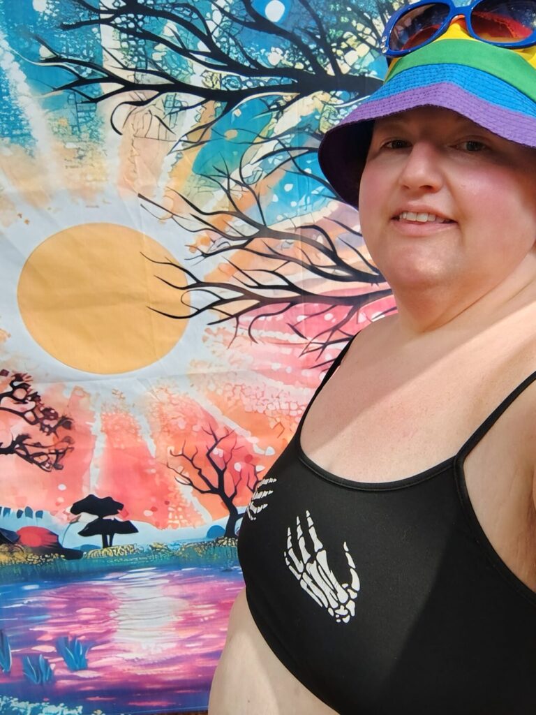 michelle anthony with black skirt and haltar and hat. Background is a river with fall leaves. 