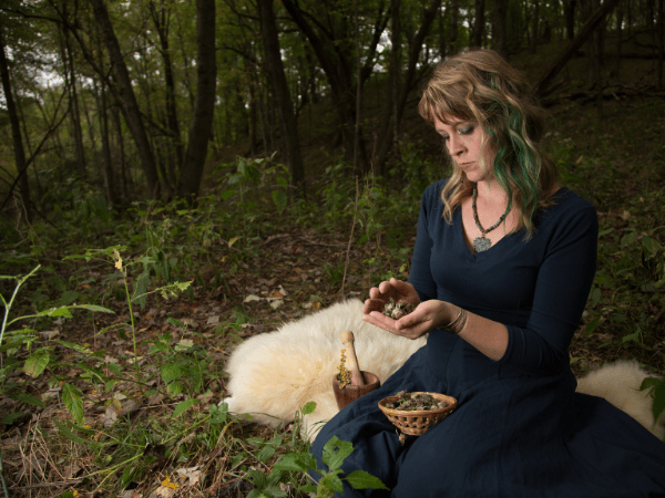 women in woods sitting, looking at her herbs 